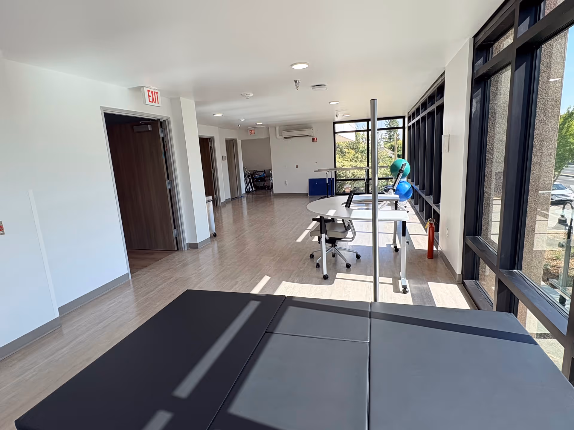 Bright interior corridor with exercise equipment and large windows in a senior living facility.