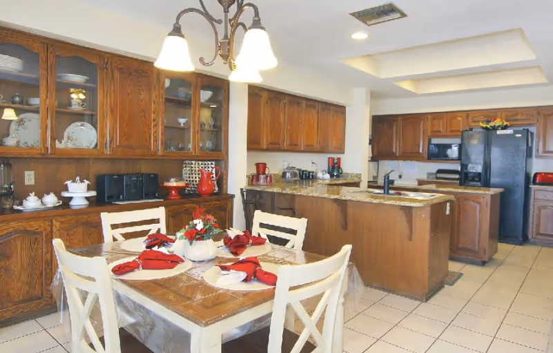 Cozy dining area with a table set for a meal, red napkins, and adjacent kitchen.