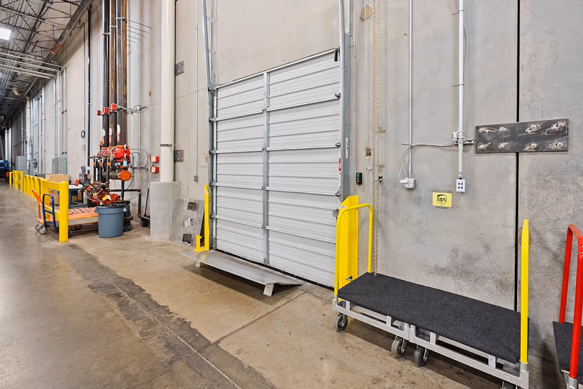 Industrial interior hallway with a large roller door, safety rails, and equipment carts.