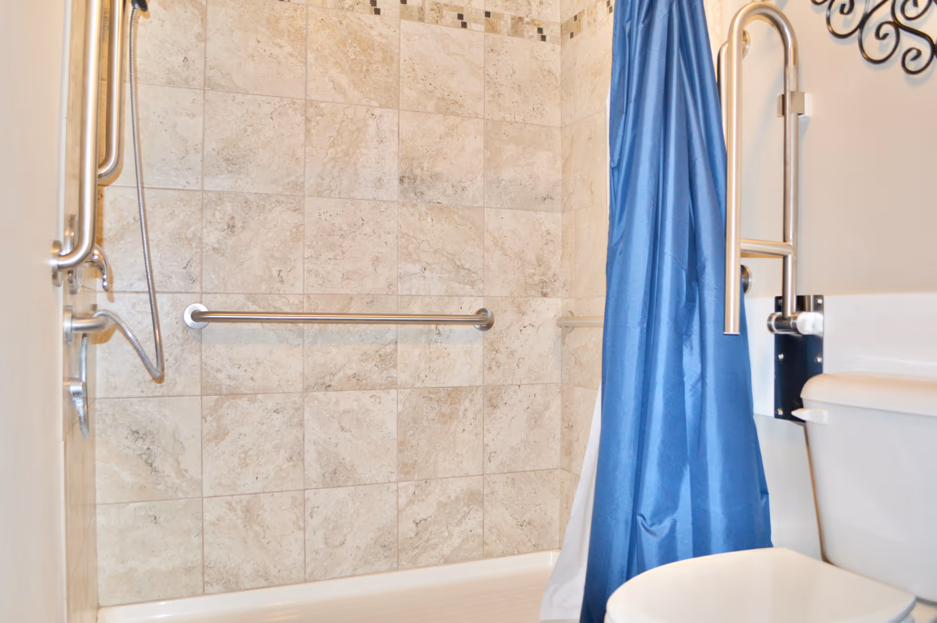 Shower area with tiled walls, grab bars, and a blue curtain in a bathroom.