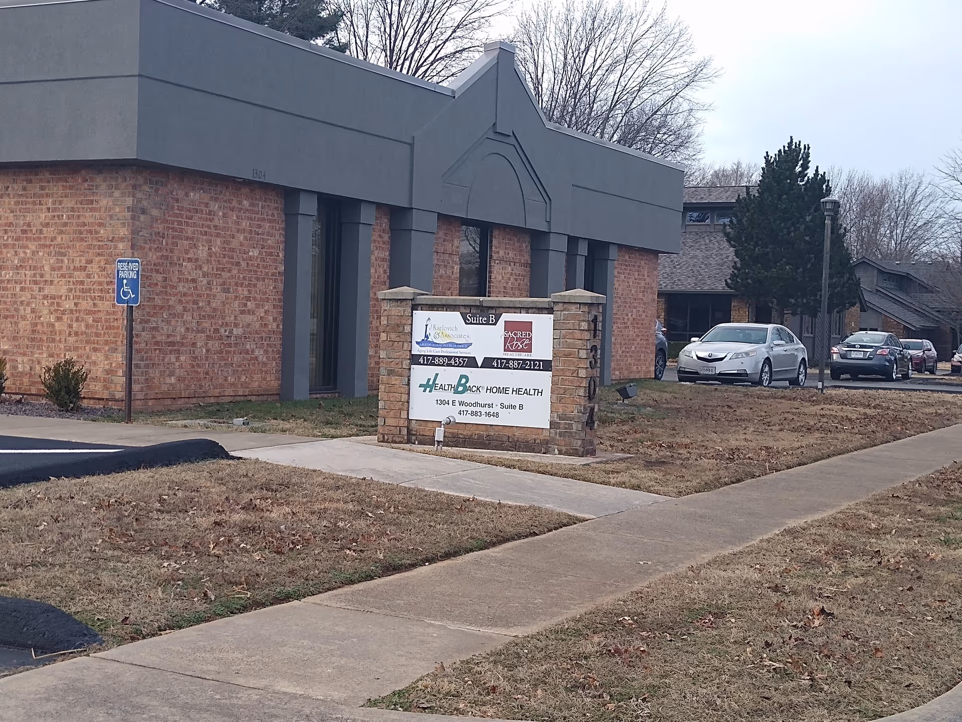 Front of Karlovich & Associates facility: brick exterior, gray facade, signboard, parked cars.