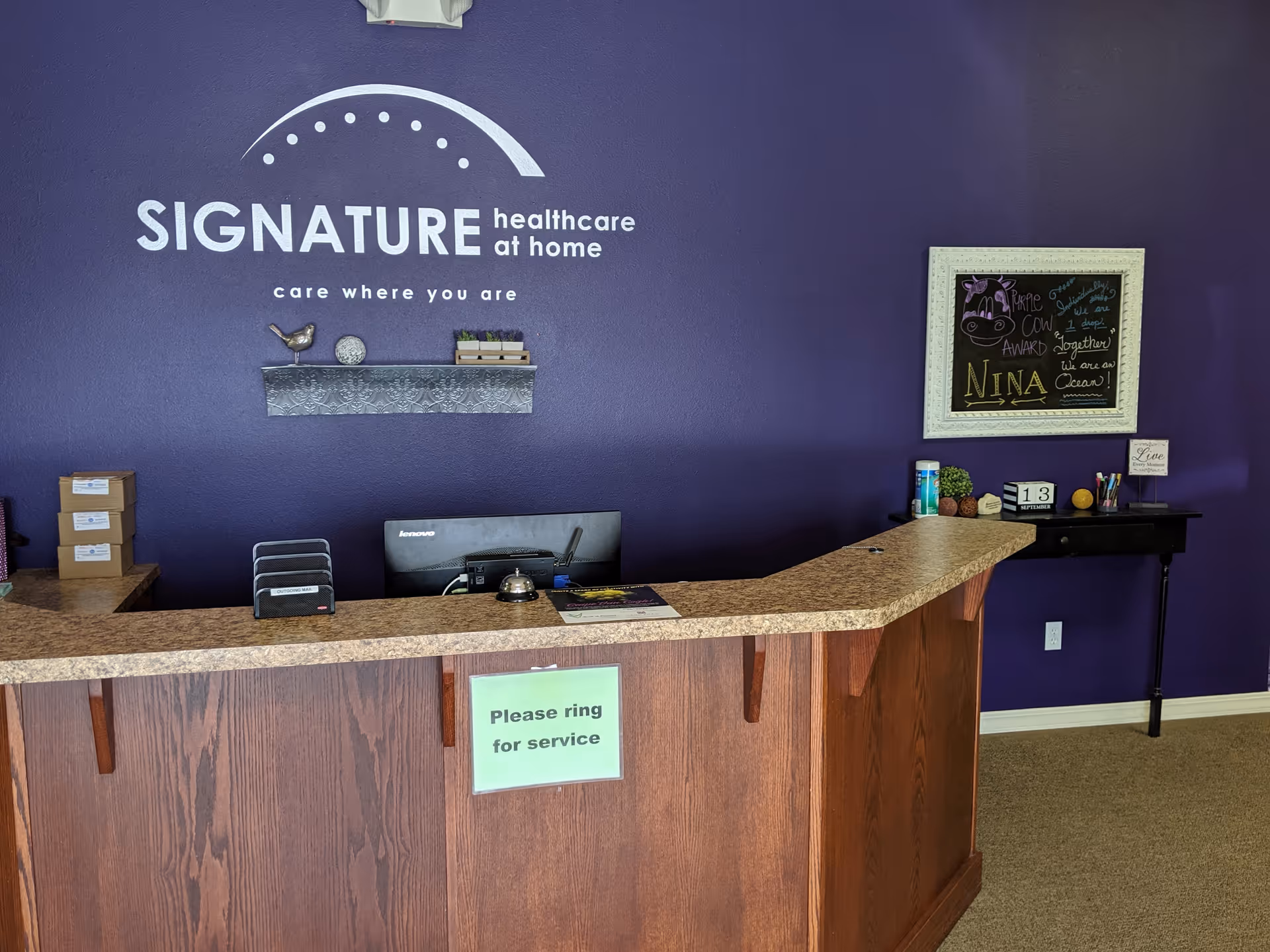 Reception desk in a purple lobby featuring the Signature HealthCare at Home logo.