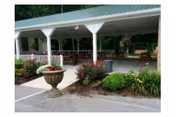 Covered outdoor seating area with white pillars, benches, and flowering shrubs in front of a building.