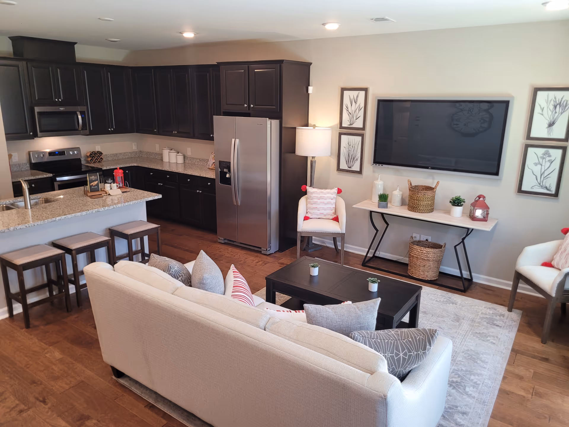 Open-concept living area featuring a beige sofa, coffee table, TV, and dark kitchen cabinets.