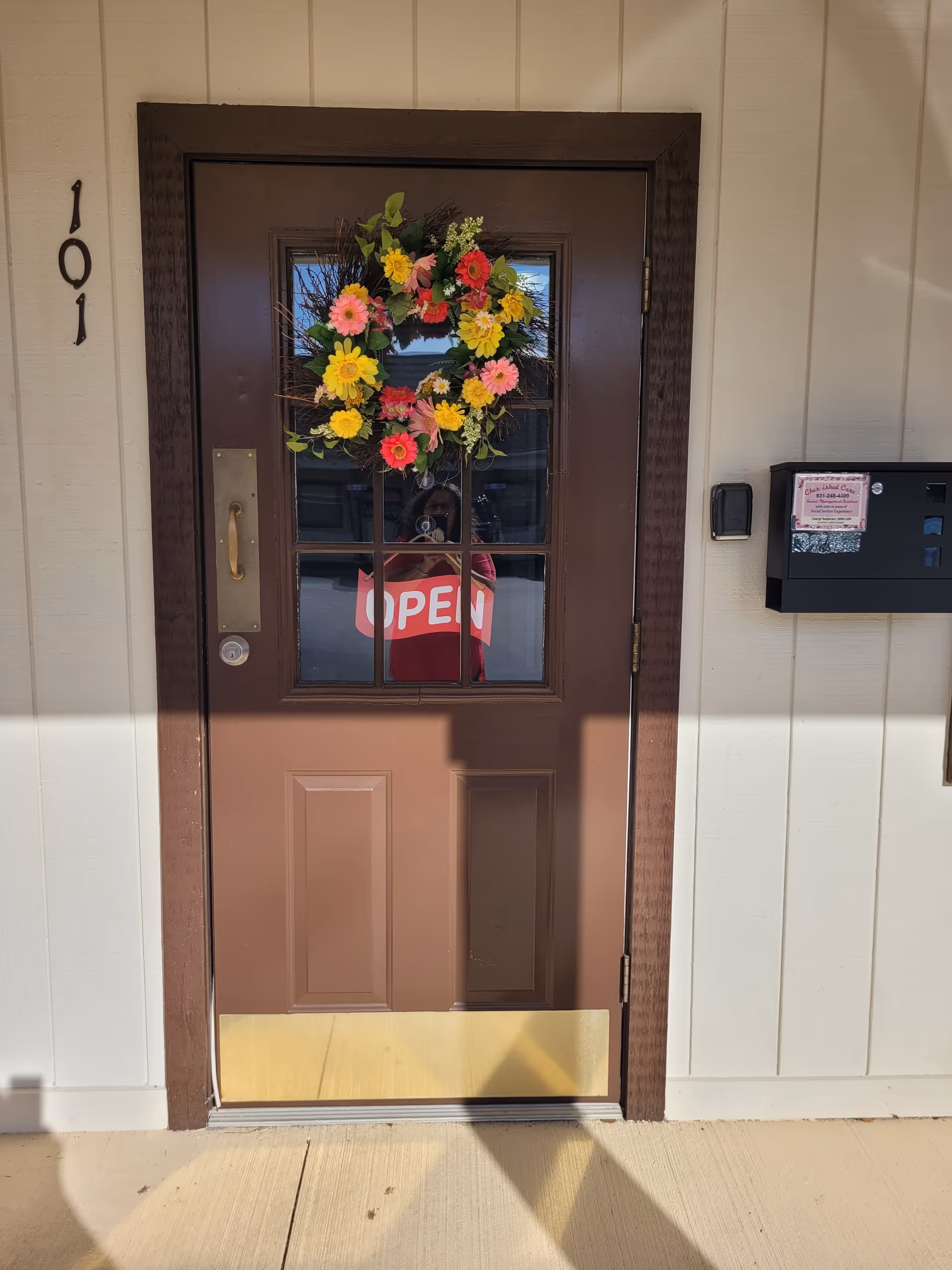 Brown front door with a colorful flower wreath and OPEN sign.