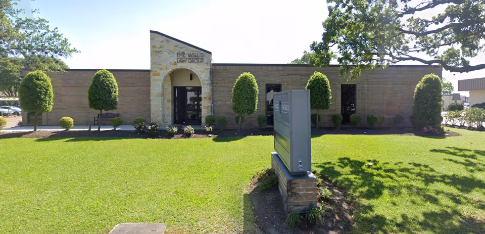 Single story brick building with arched front entrance, manicured lawn, trimmed trees, and a sign.