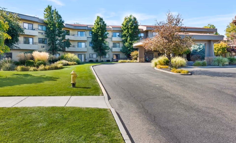 Exterior view of a multi-story senior living facility with driveway and landscaped lawn.