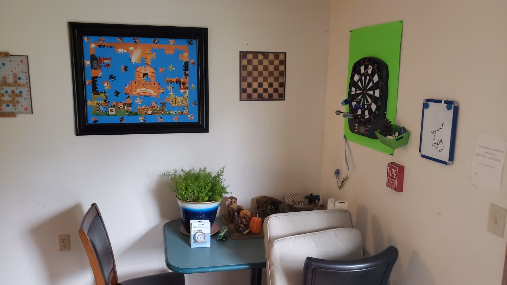 Small activity room with a table, chairs, plant, and a wall-mounted dartboard.