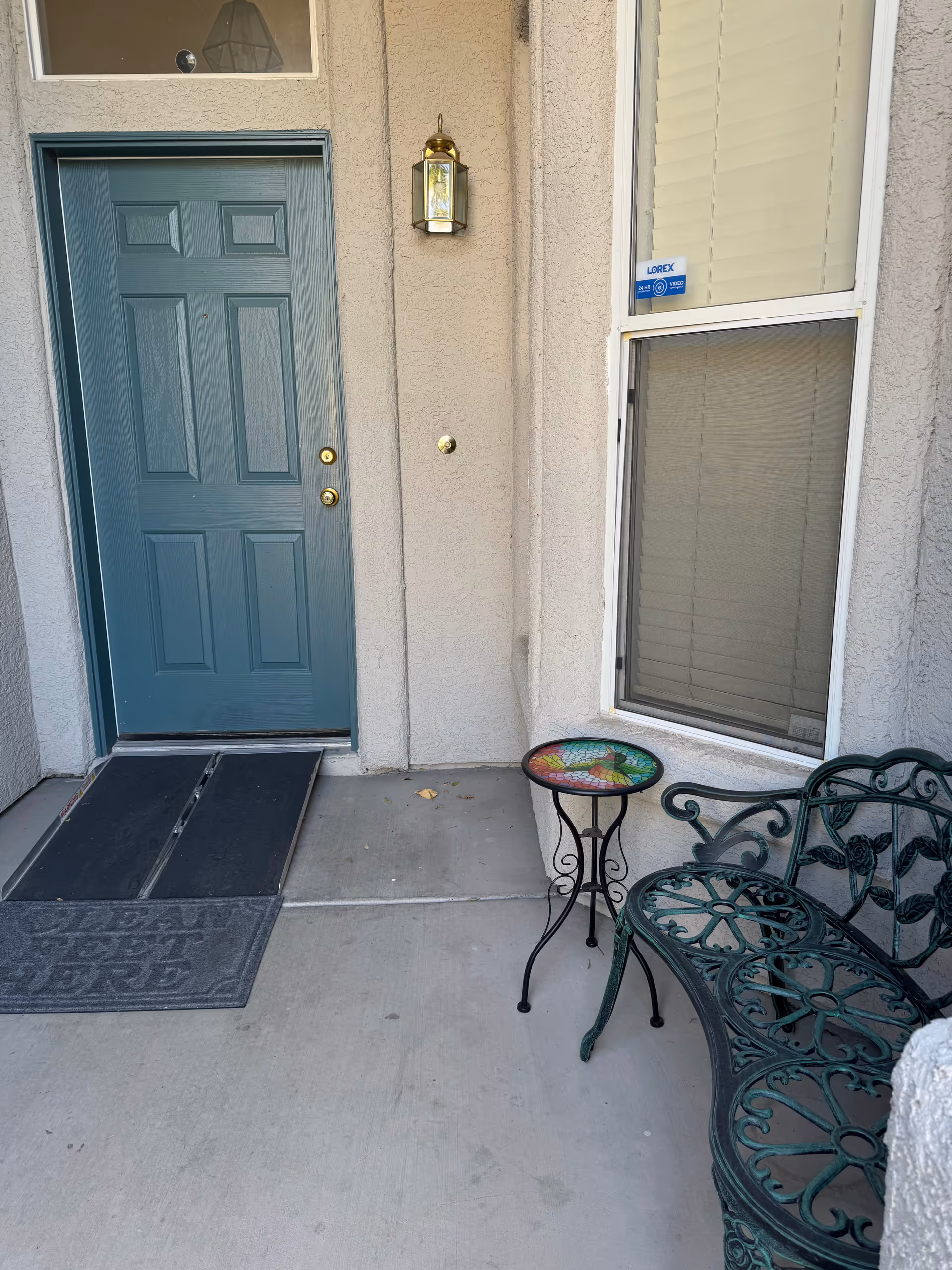 Front entrance of a building with teal door, window, and metal seating.