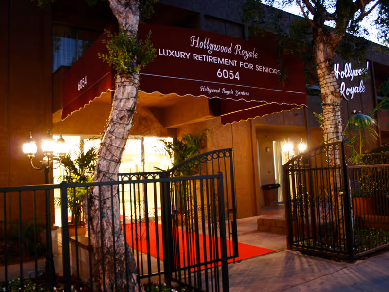 Entrance of Hollywood Royale Gardens retirement facility with a maroon awning, red carpet and wrought-iron gates.