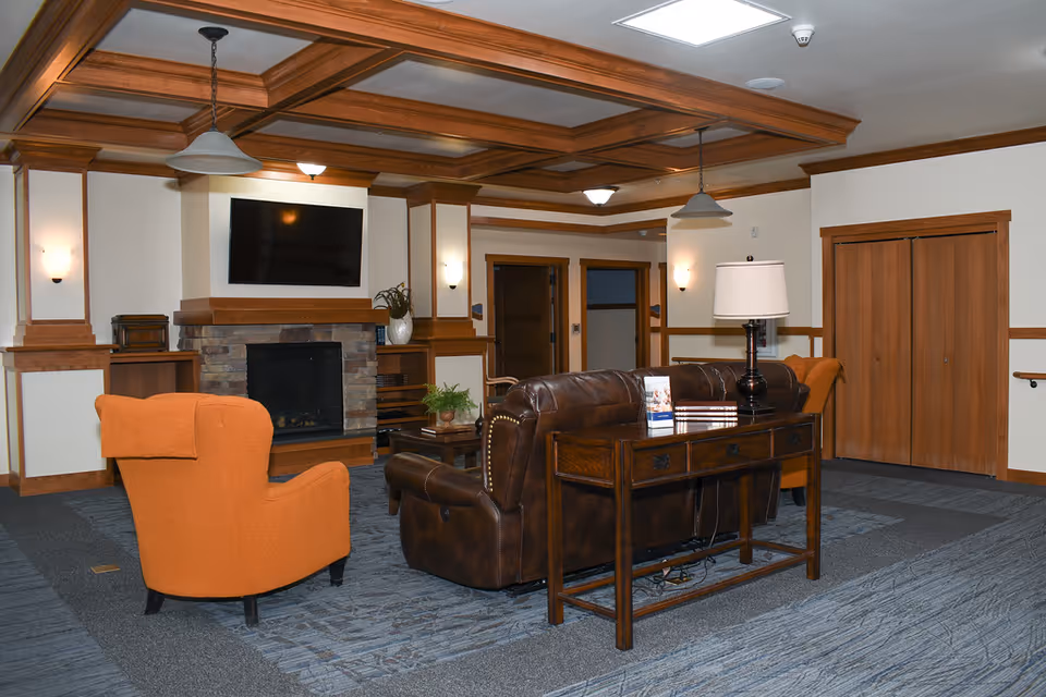 Spacious resident lounge with leather seating, an orange chair, fireplace, and wall-mounted TV.