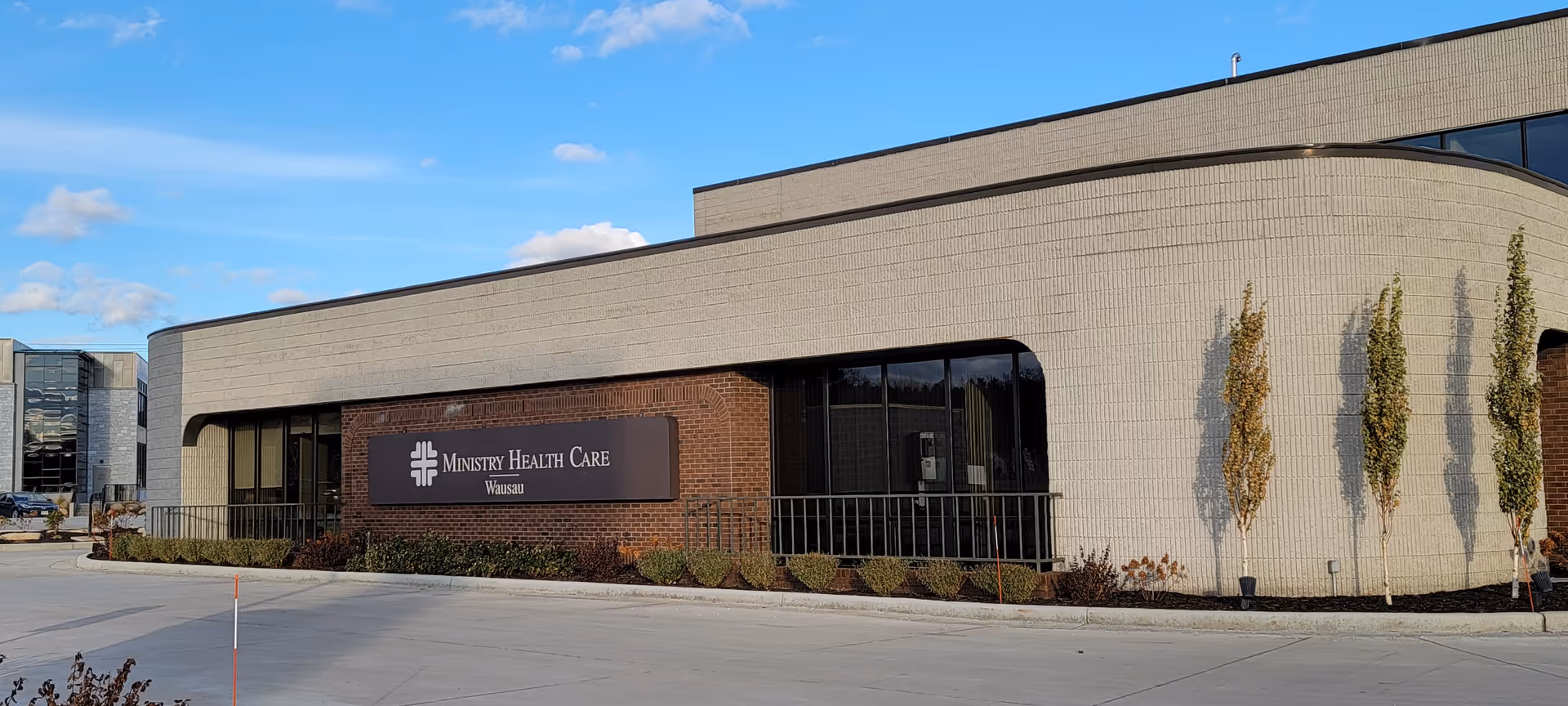 Modern health care facility exterior with a brick sign and curved light-tan walls.