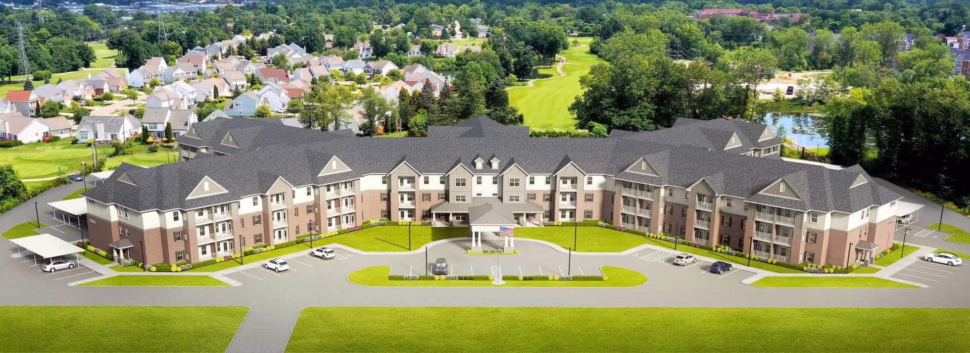 Aerial view of a large, multi-story senior living facility named American House Village At Bloomfield, surrounded by green lawns and trees, with a driveway and several parked cars in front. Residential houses and a golf course are visible in the background.