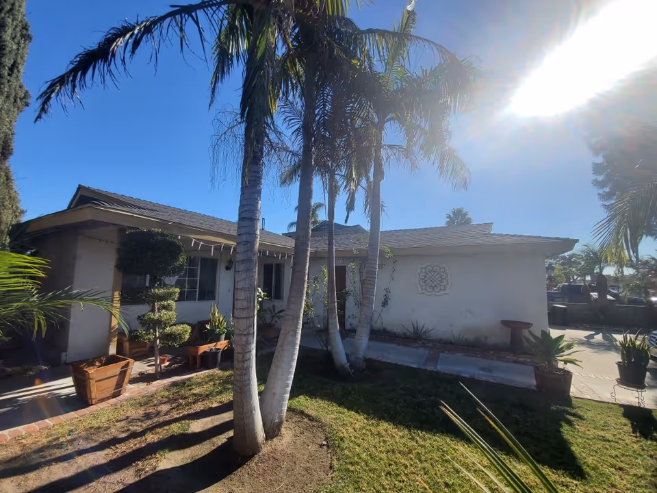 Exterior view of a single-story senior living facility with palm trees and potted plants.