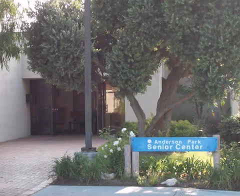 Entrance to a senior center with a sign reading Anderson Park Senior Center, flanked by trees.