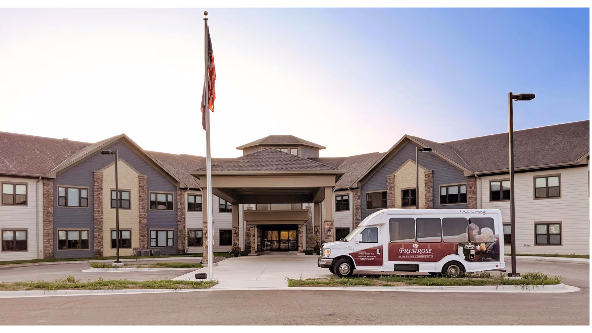 Front exterior of Primrose Retirement Community with an entrance canopy, flagpole, and a Primrose shuttle van parked in front.