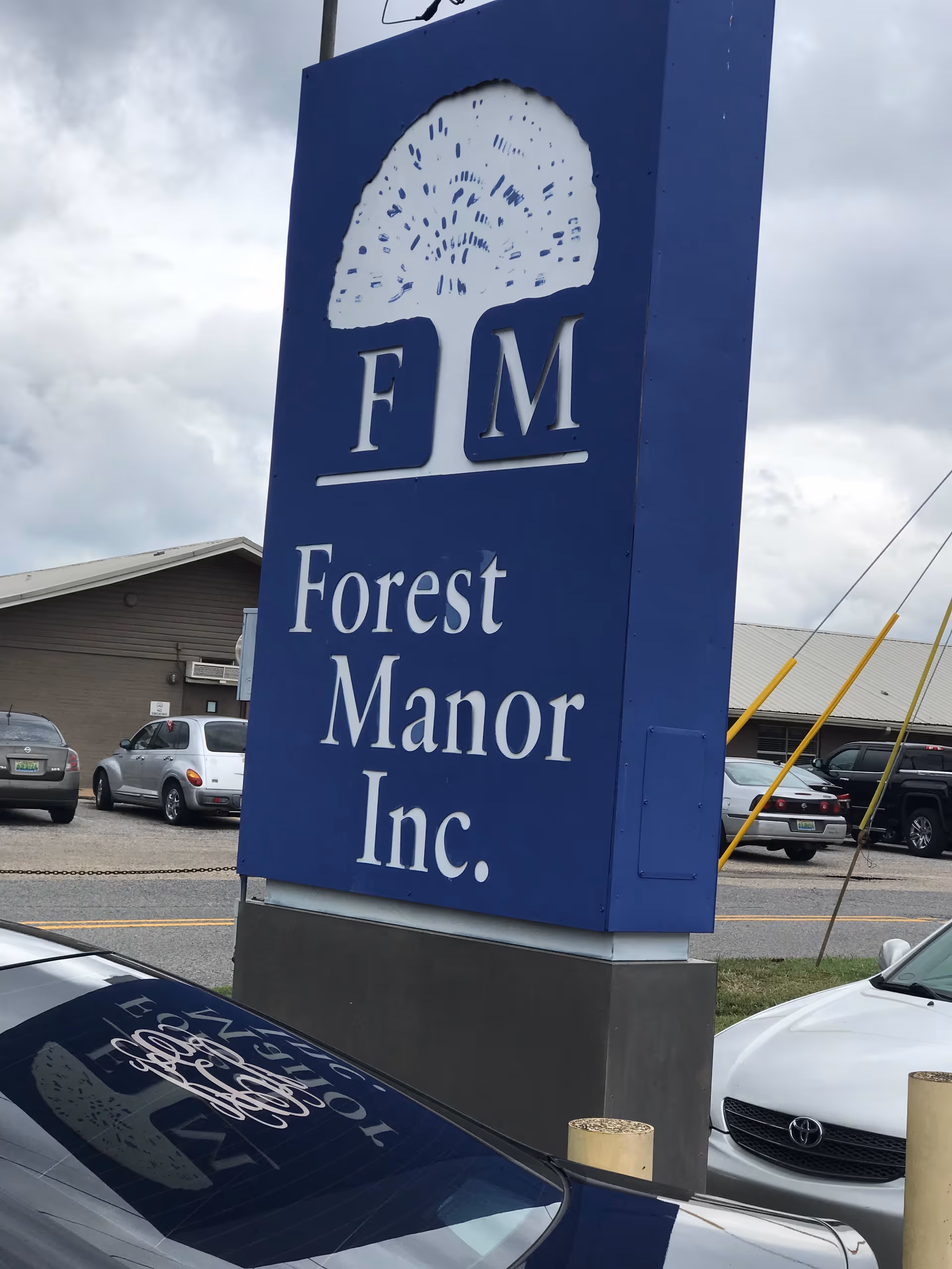Tall blue sign reading Forest Manor Inc. with logo in a parking lot.