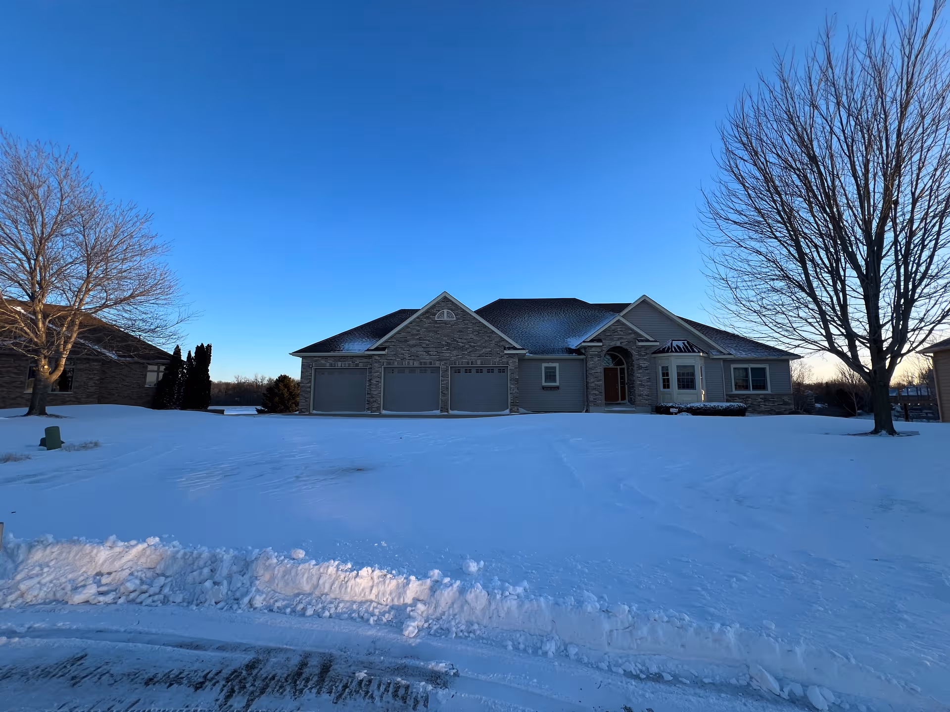 Snow-covered single-story senior living facility with stone facade and three-car garage under blue sky.
