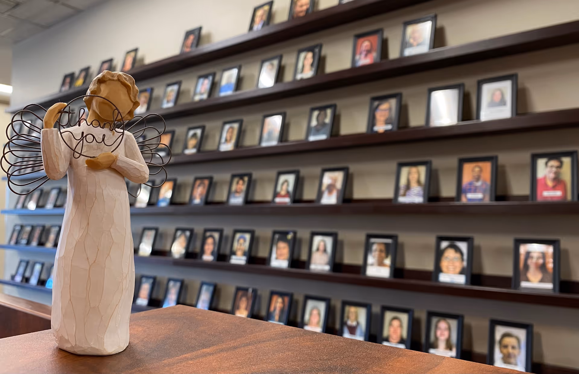 Wooden angel sculpture with thank you wire wings on a table; framed resident photos line shelves.