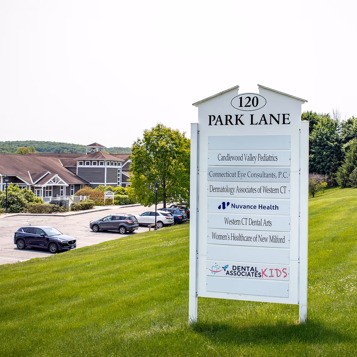 Outdoor Park Lane signboard lists medical practices, with a grassy lawn and parked cars.