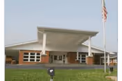 Front exterior of a single-story brick building with a large covered entrance and flagpole.