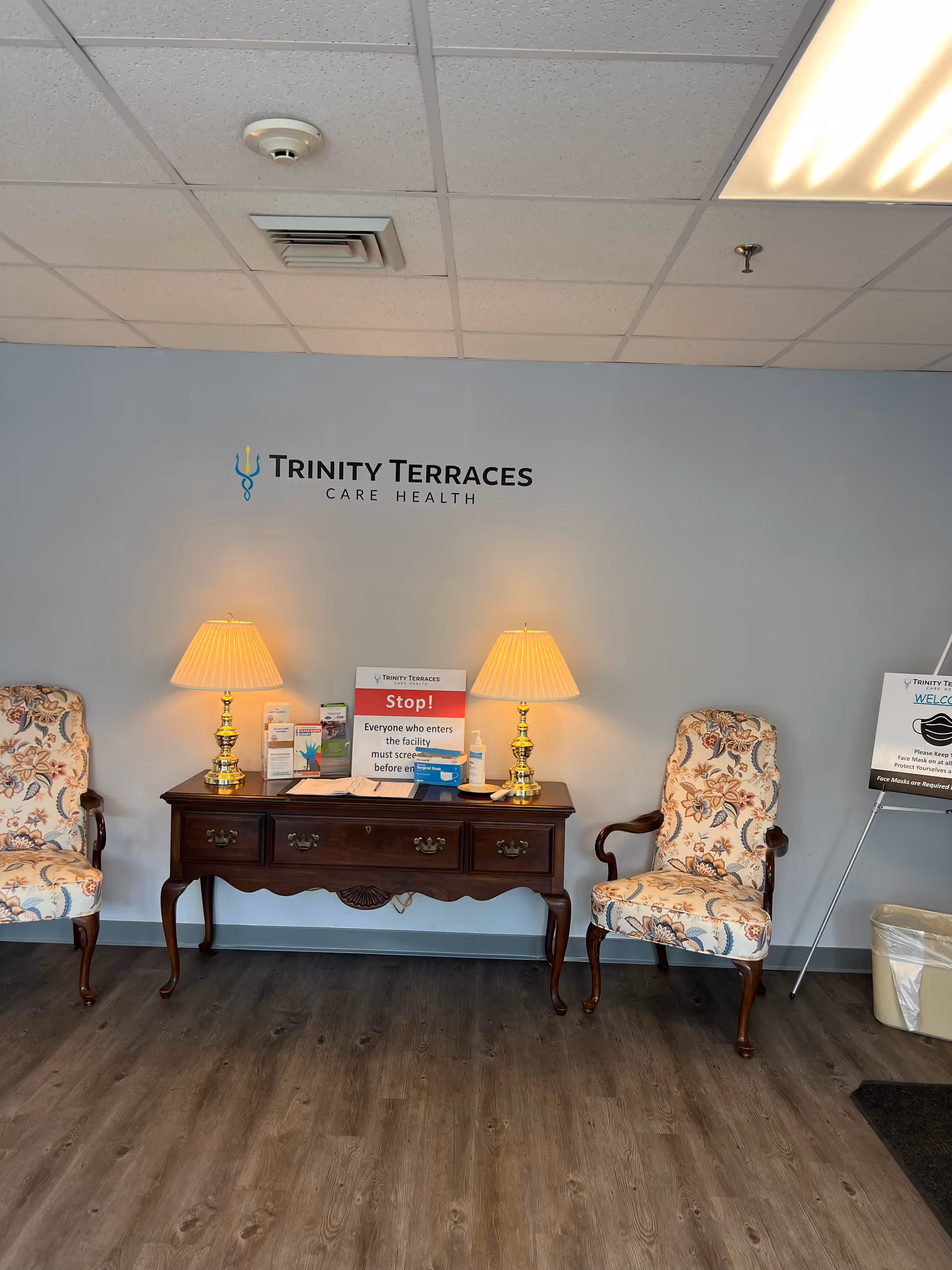 Reception area with a console table, two patterned chairs, and Trinity Terraces sign.