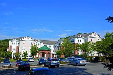 Exterior view of Rose Tree Place senior living facility with parked cars and trees.