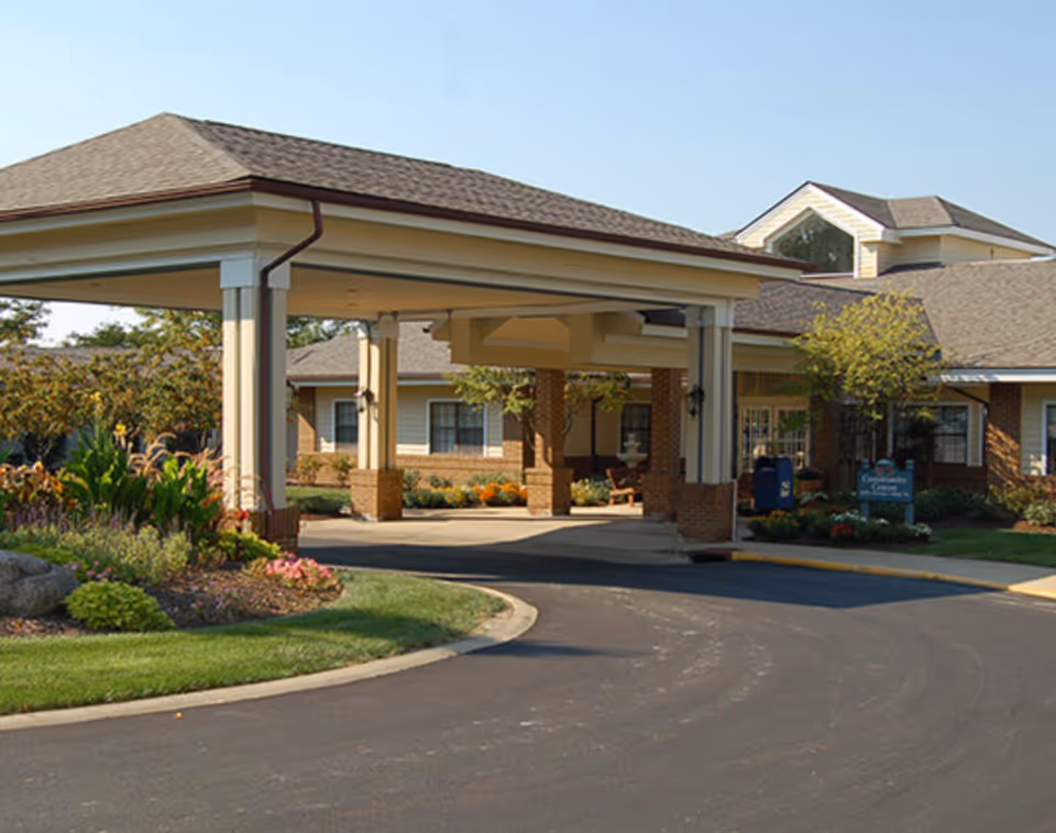 Covered porte-cochere entrance of a senior living facility with landscaped beds and a circular driveway.