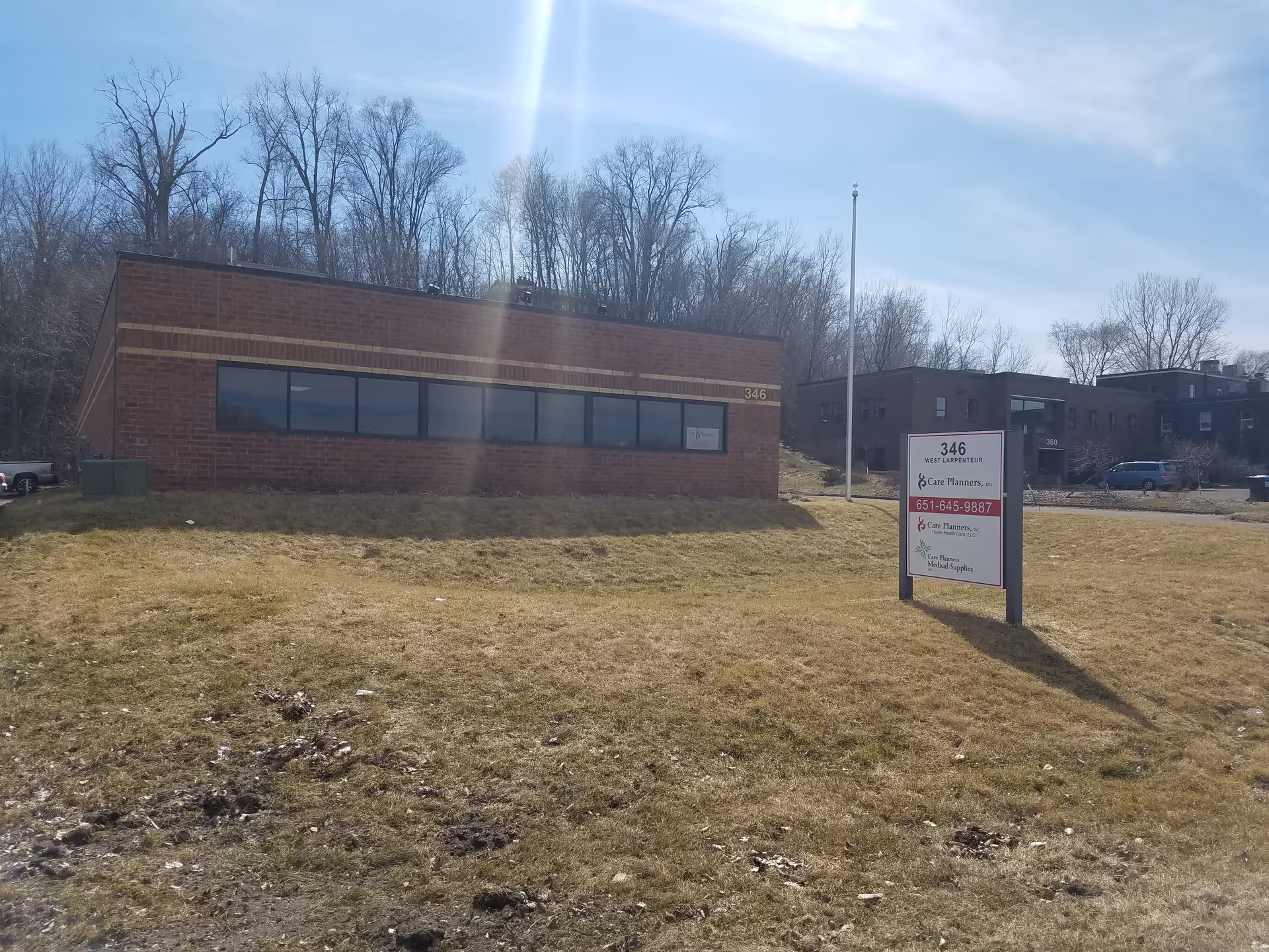 Brick building exterior with a sign in a grassy lot and bare trees behind.