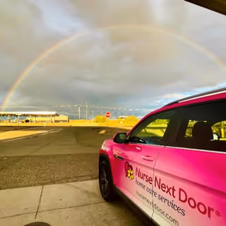 Pink Nurse Next Door van parked in a lot under a double rainbow.