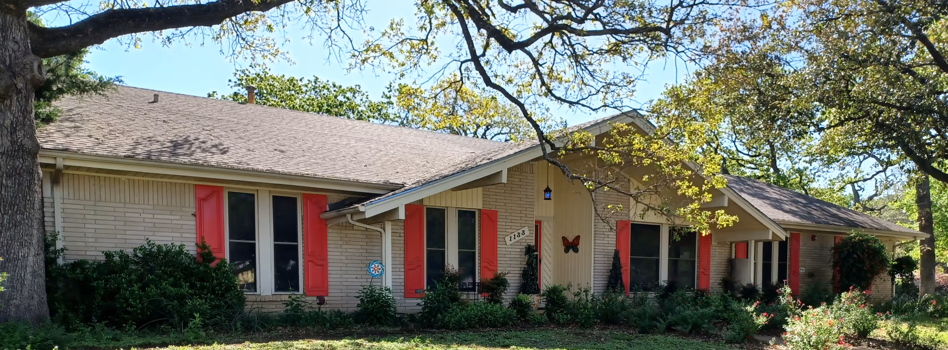 Single-story beige brick senior care home with red shutters and landscaped front yard.