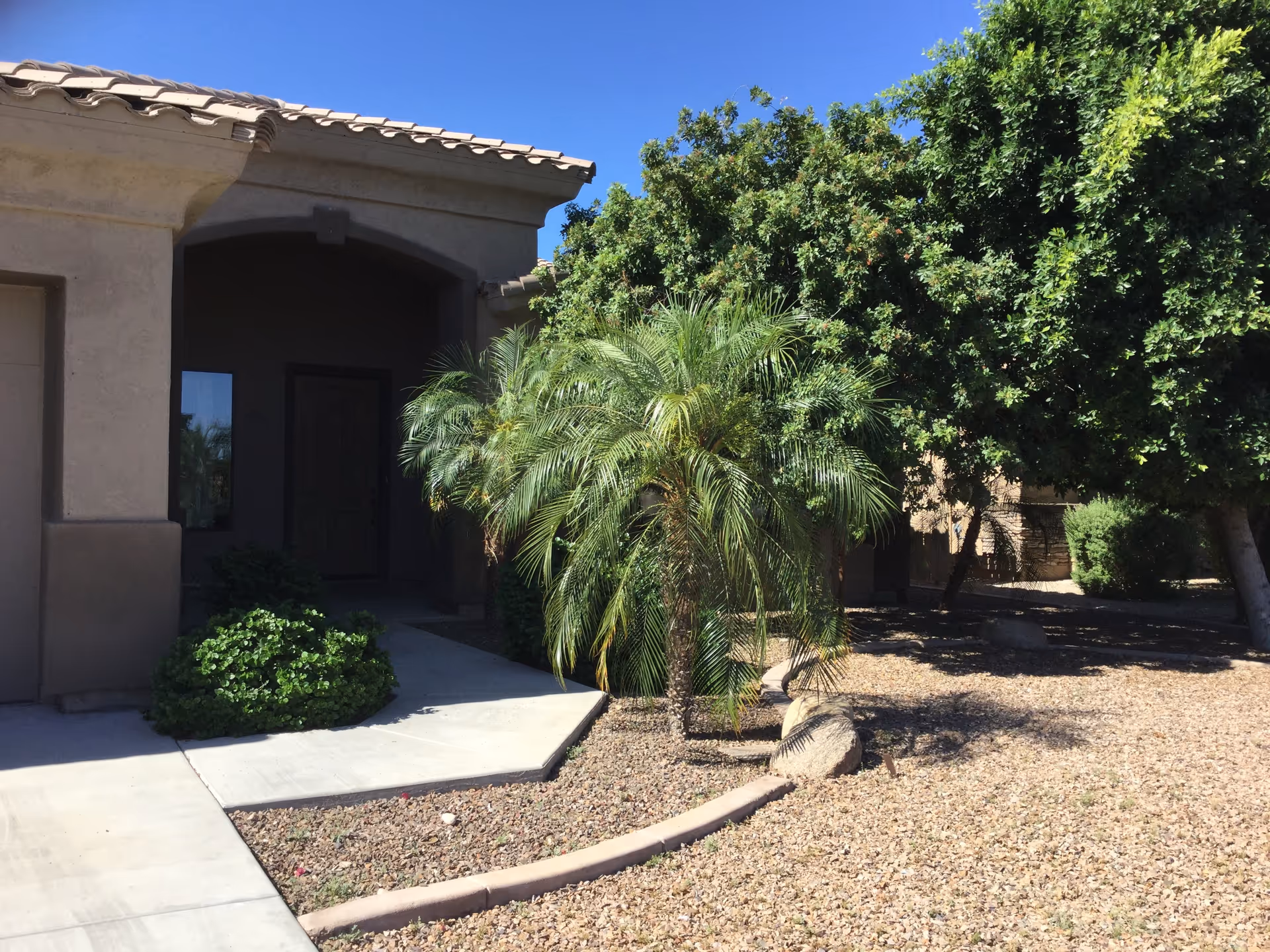 Front entrance of a beige residential care home with desert landscaping and palm trees.