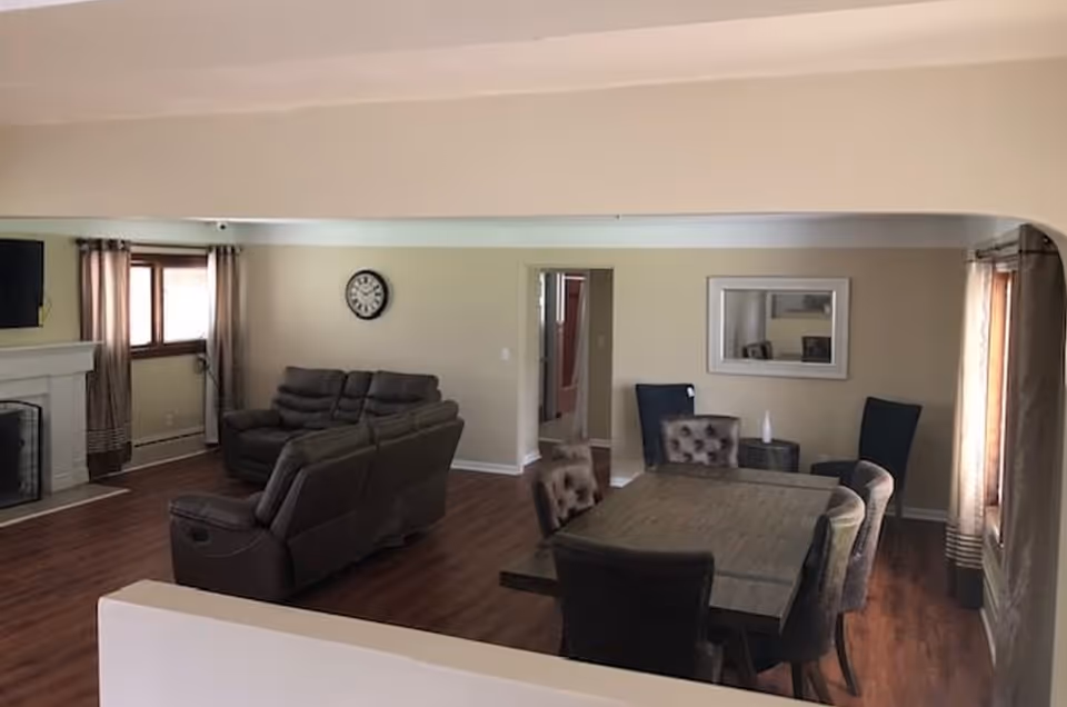 Open living area with fireplace, beige walls, and a dining table with upholstered chairs.