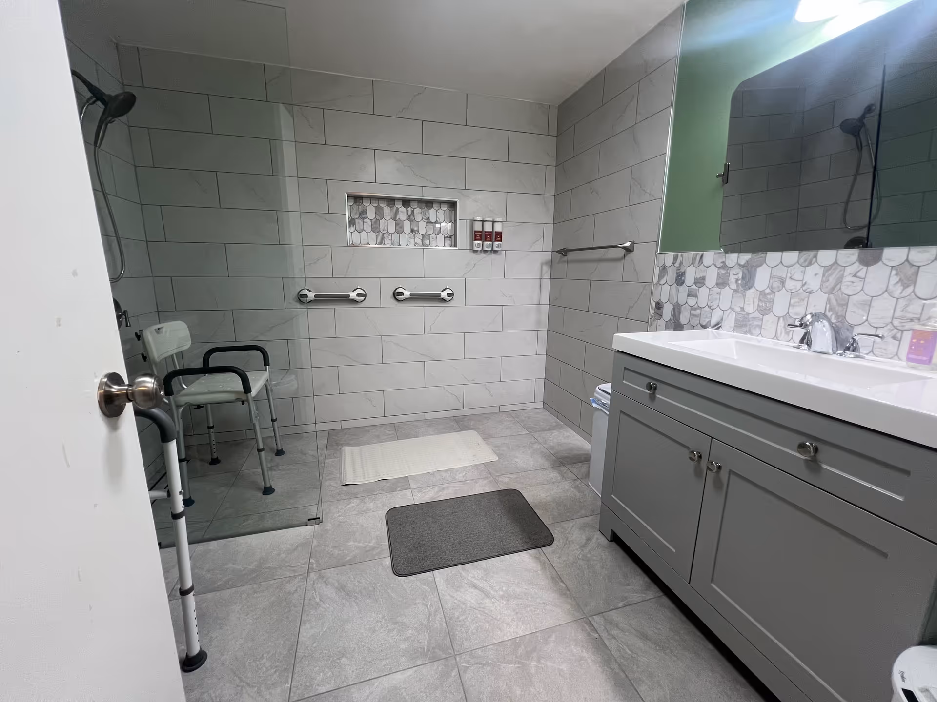 Accessible bathroom with shower chair, grab bars, walker, and gray vanity.