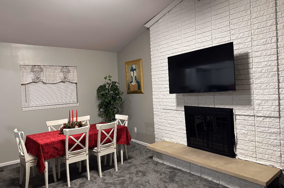 Dining area with a red-cloth table, white chairs, fireplace, and wall-mounted TV.