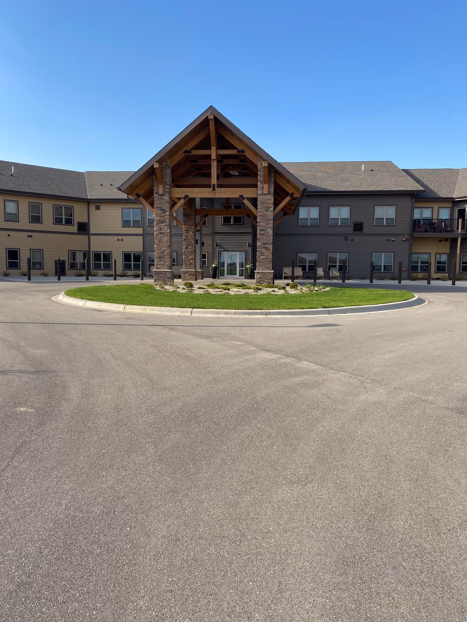 Modern senior living building with a stone-front entrance and wooden peaked canopy.