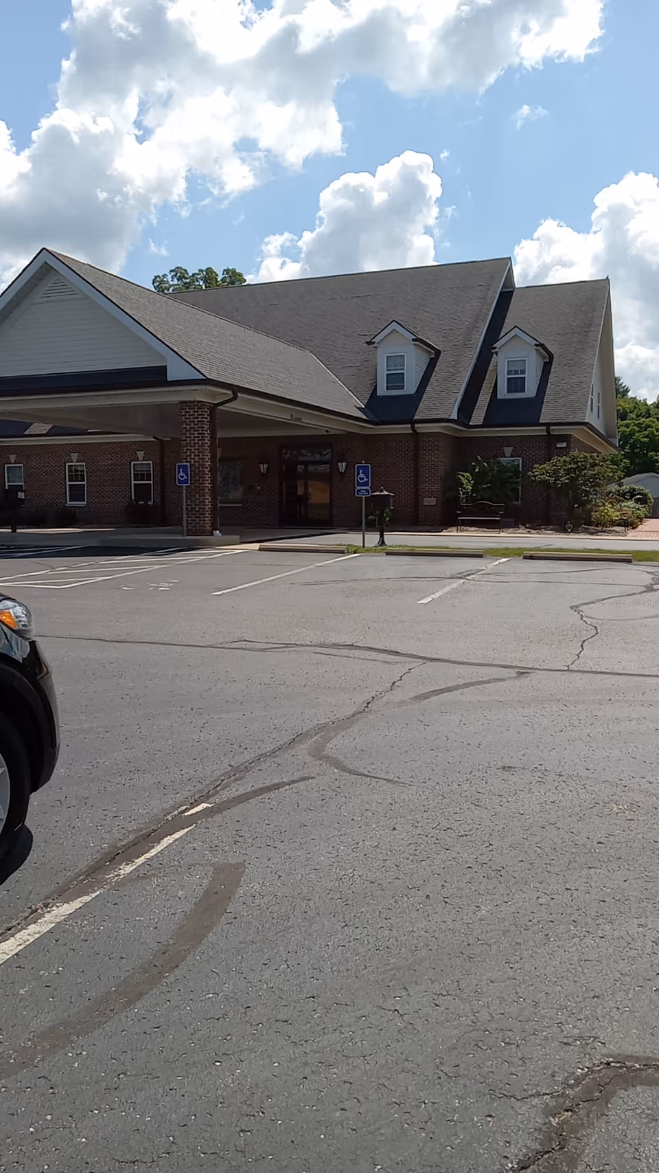 Brick senior living facility exterior with peaked-roof entrance and parking lot.