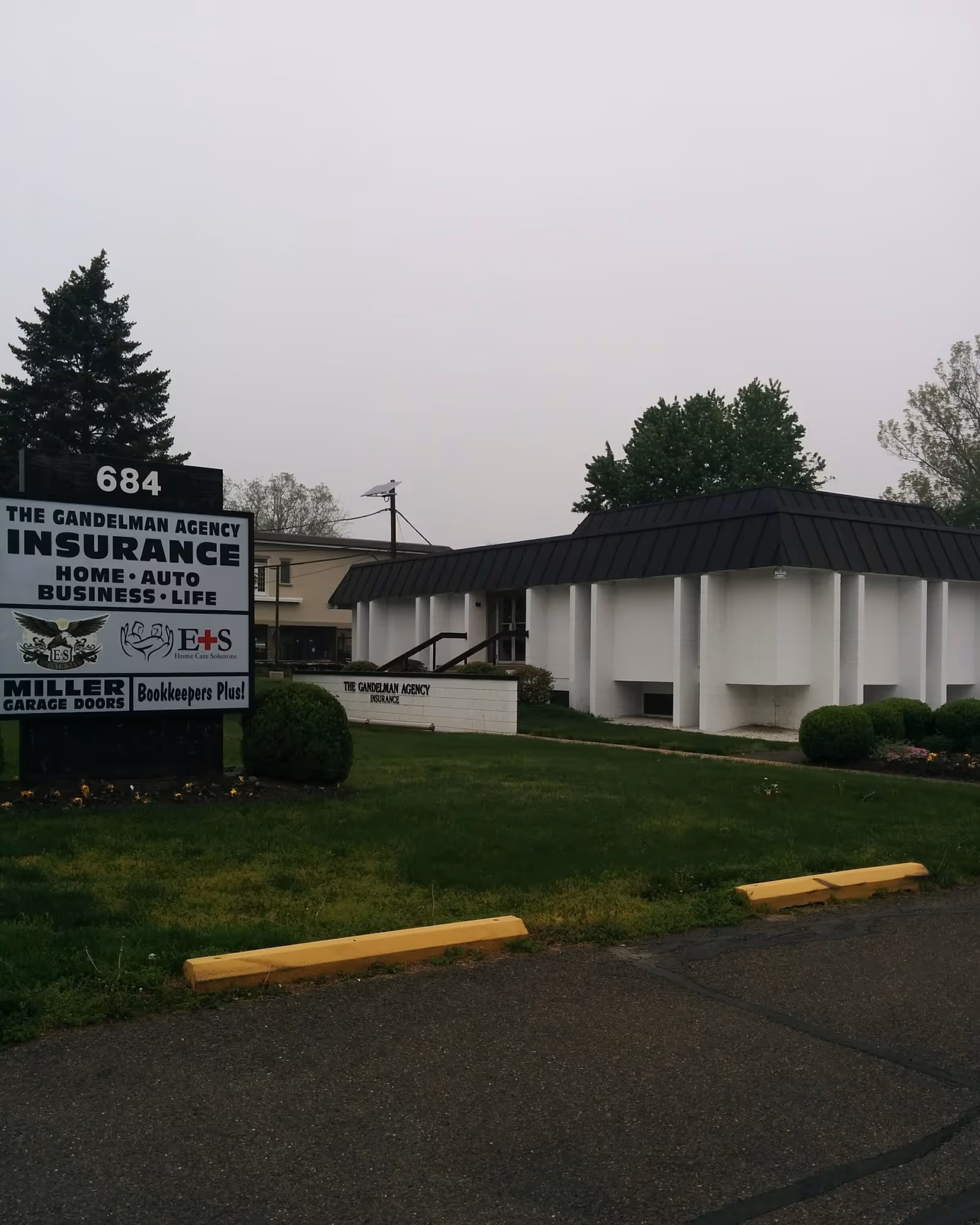 Exterior of a white low-rise building with a black roof and prominent lawn sign.