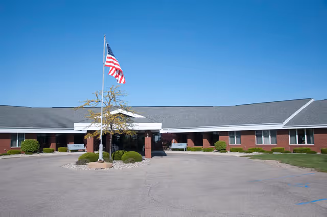 Exterior view of a single-story brick senior care facility with a waving American flag