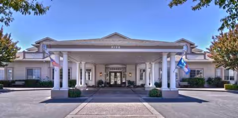 Front entrance of Ivy Park at San Ramon with columns and flags under a clear sky.