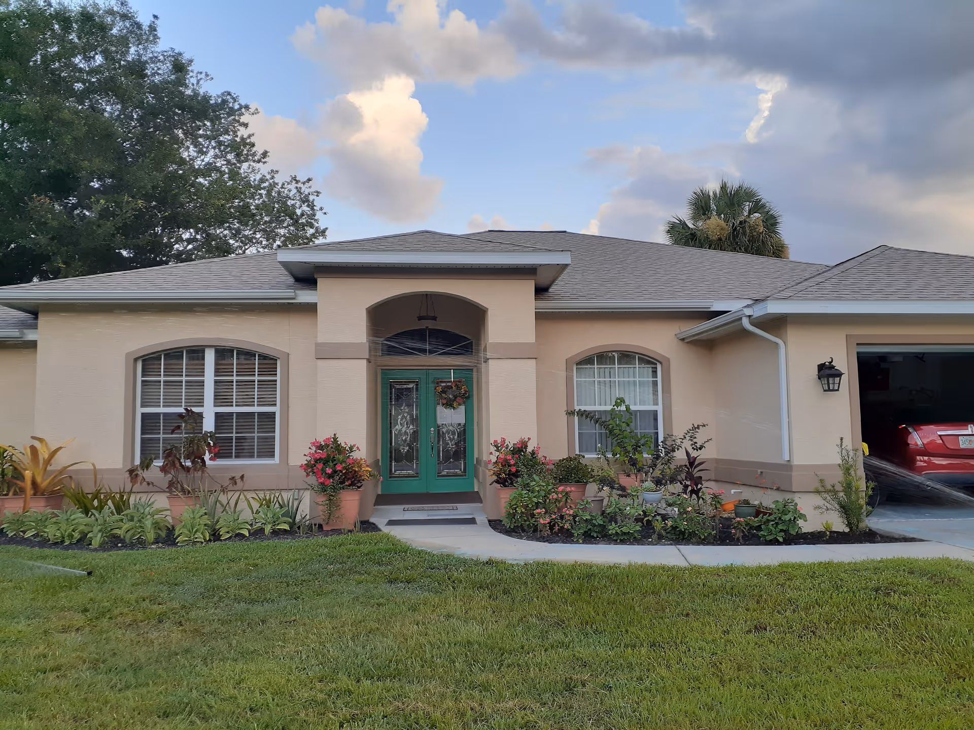 Front exterior of a single-story beige house with green double doors, potted plants, and an attached garage.