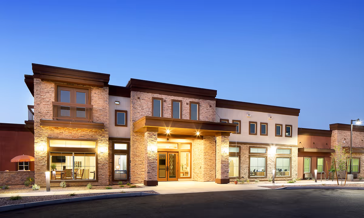 Modern senior living facility exterior at dusk with stone columns and a lit entrance.