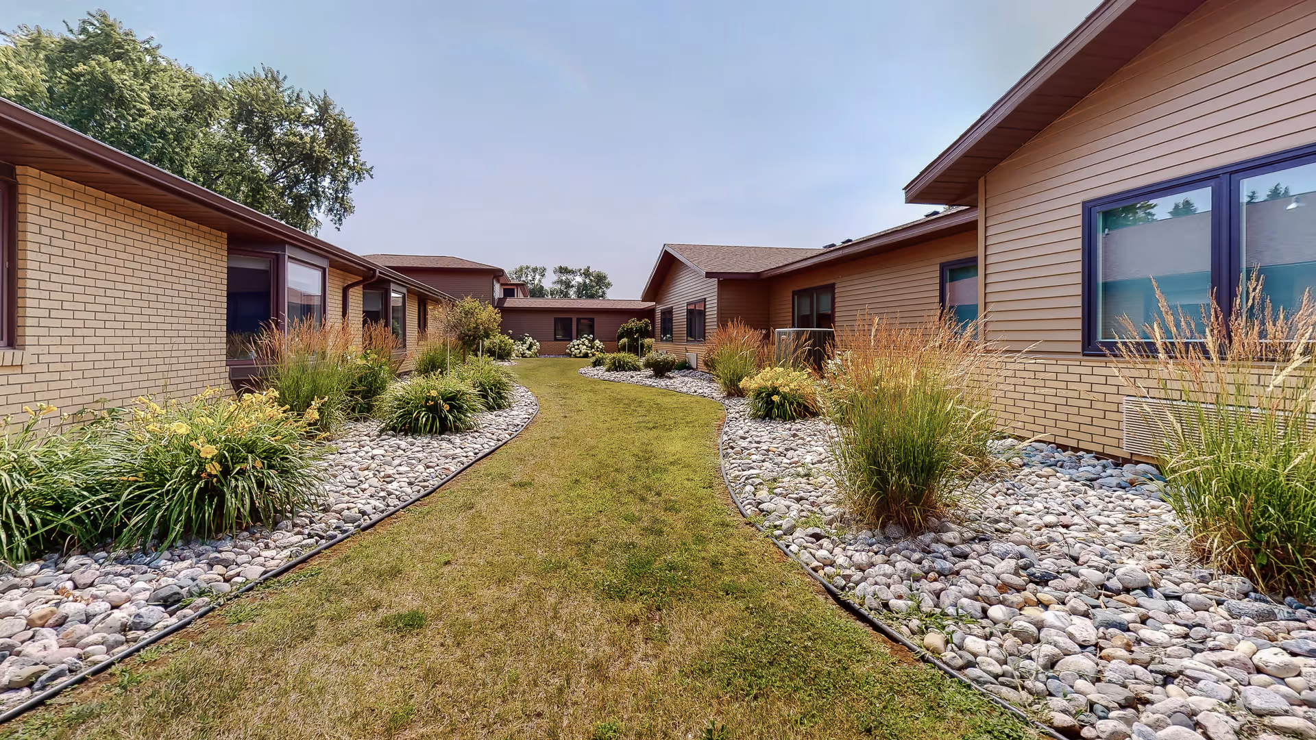 Exterior view of Hatton Prairie Village showing low-rise buildings, a grassy central path, and rock landscaping.