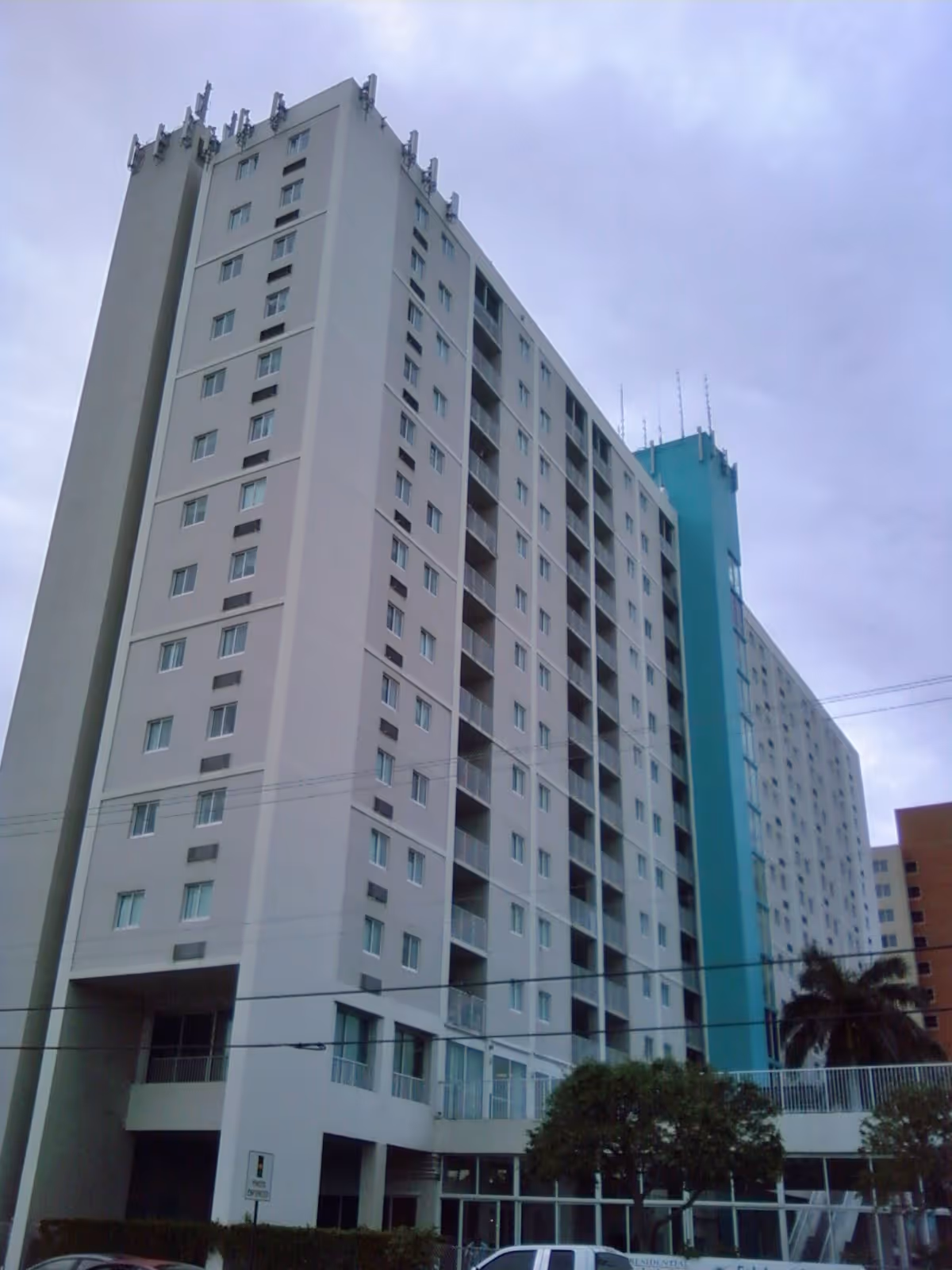 Tall white high-rise residential building with balconies and blue accents under a cloudy sky