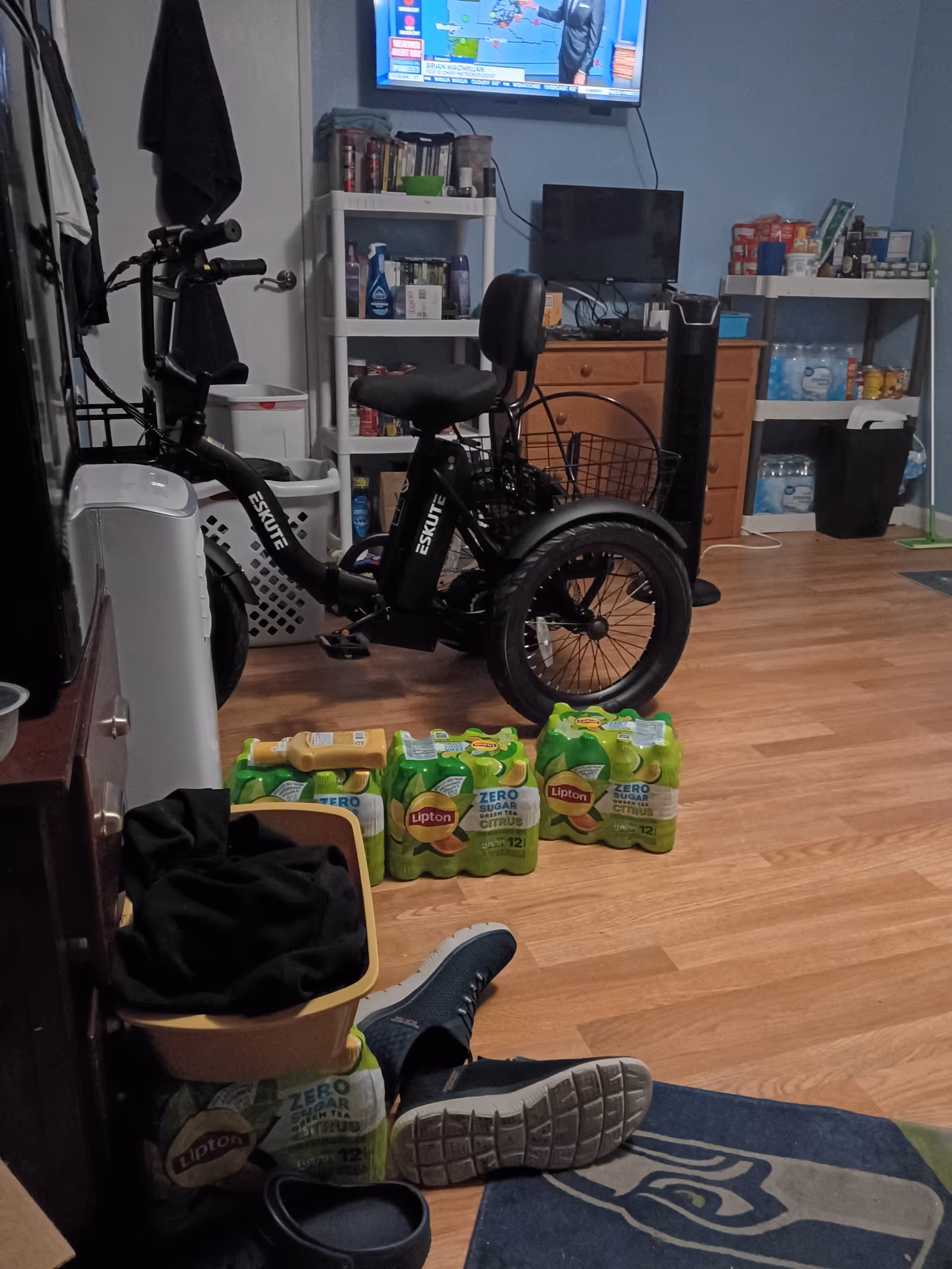 Interior room with a stationary bike, shelves of supplies, and Lipton drink packs on the floor.