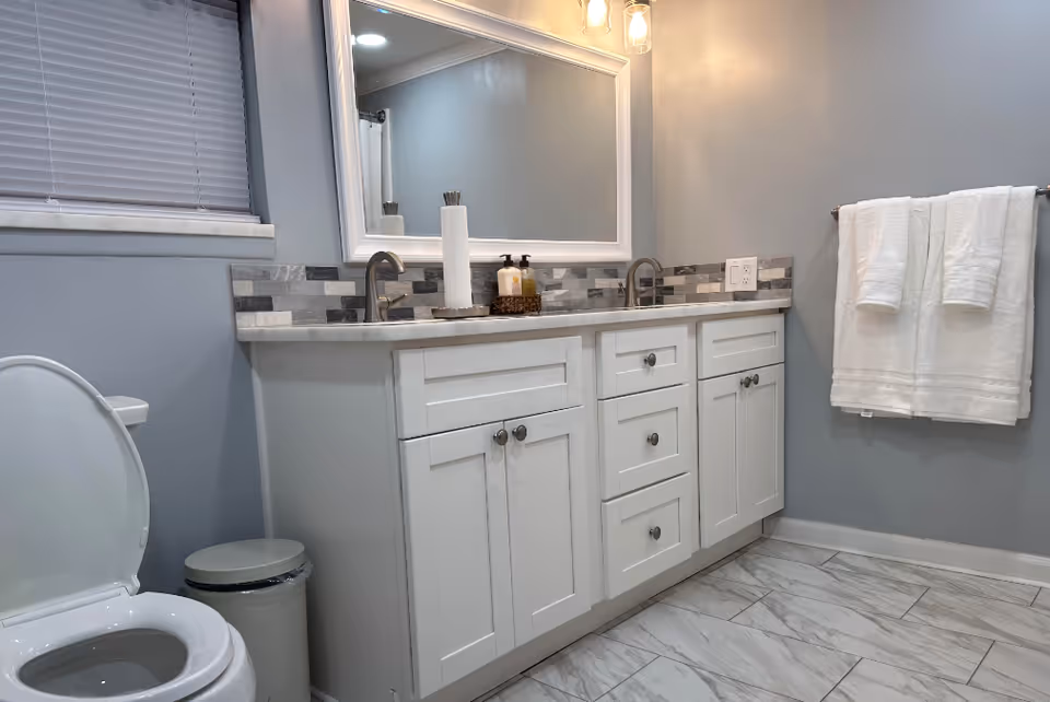 Modern bathroom with double sink vanity, toilet, tiled floor, and towel rack.