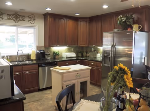Dark wood kitchen cabinets surround stainless appliances, a small island, and a sunflower centerpiece.