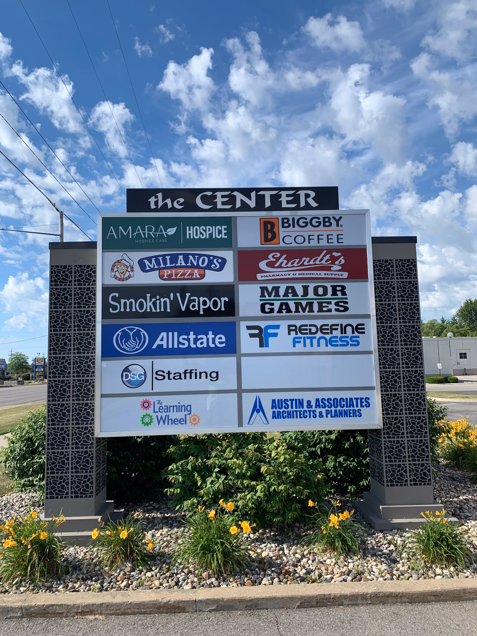 A large outdoor signboard with multiple business logos at a shopping center.