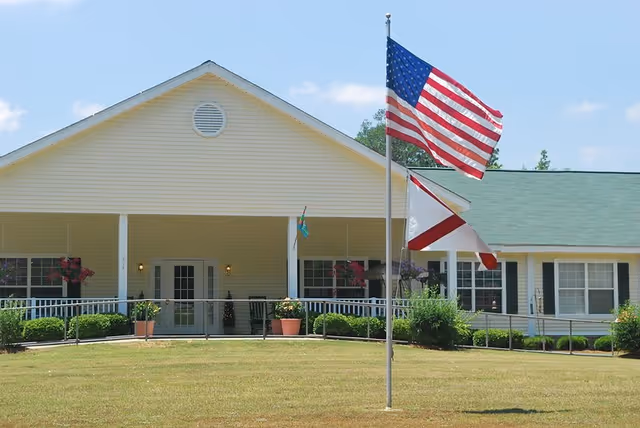 Gardens of Clanton senior living facility front: yellow building, covered porch, flags on lawn