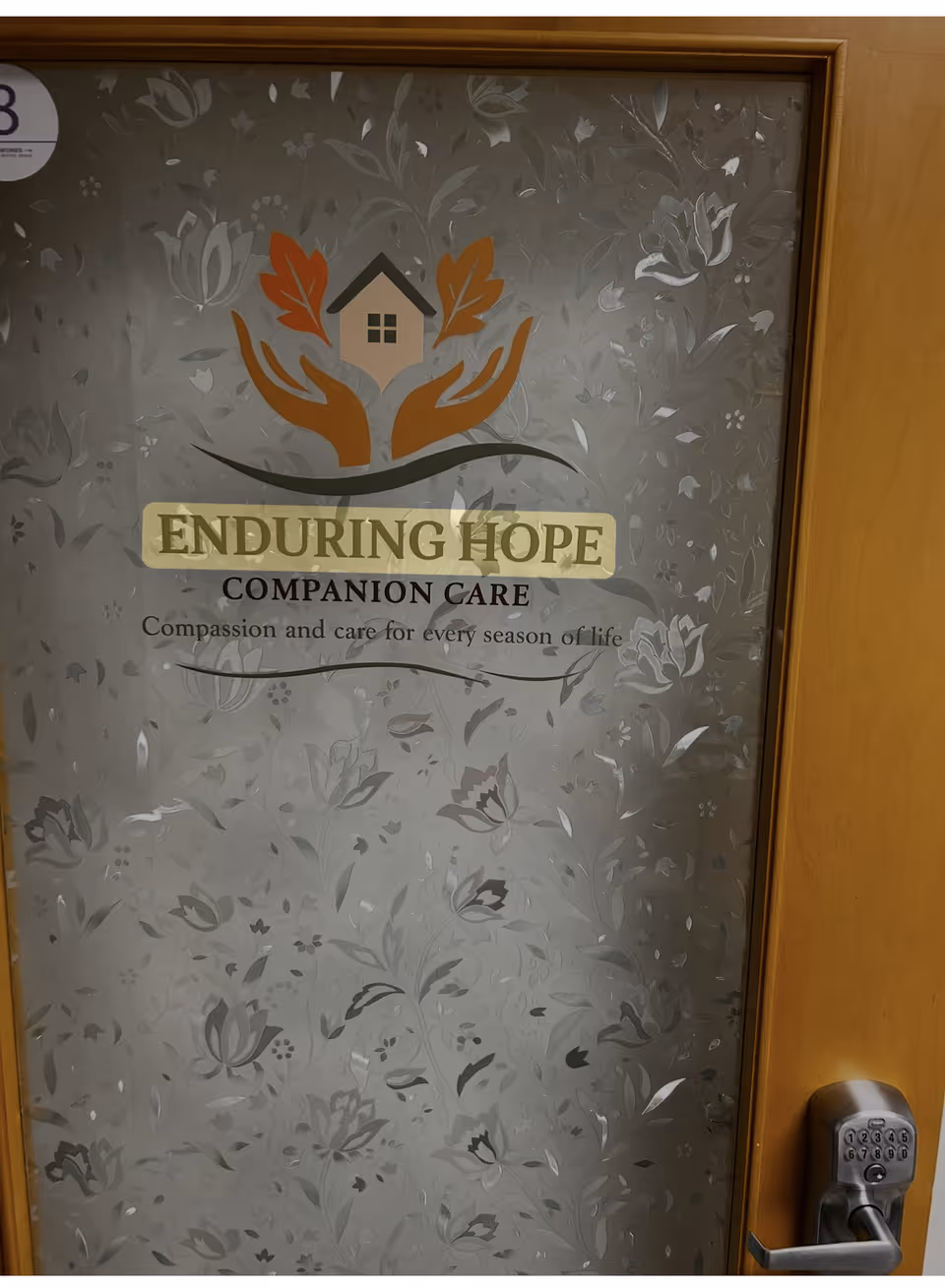 Interior door displaying Enduring Hope Companion Care logo amid patterned wallpaper and a metal handle.